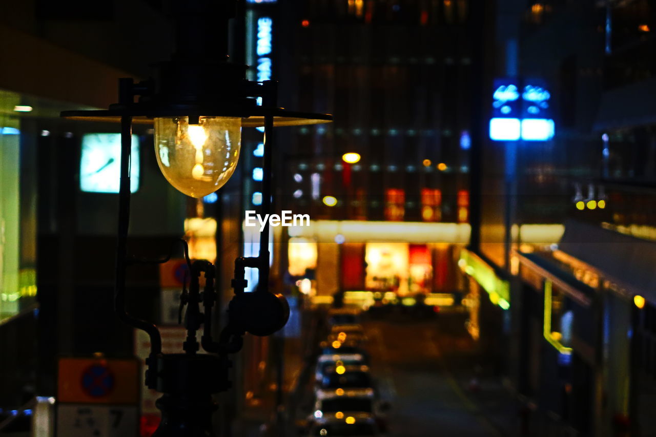ILLUMINATED LIGHTS ON STREET AMIDST BUILDINGS AT NIGHT