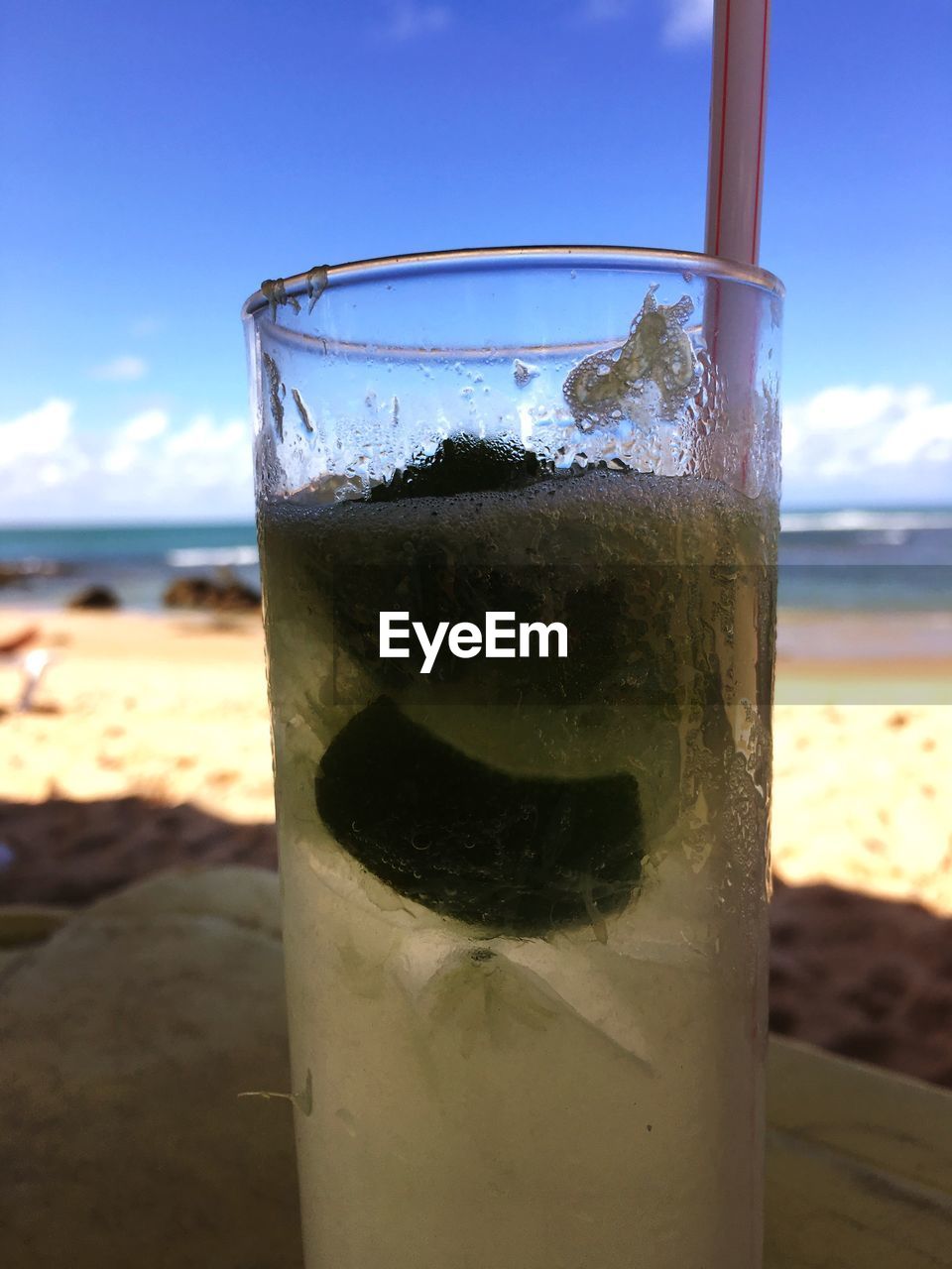 CLOSE-UP OF DRINK ON BEACH AGAINST SKY