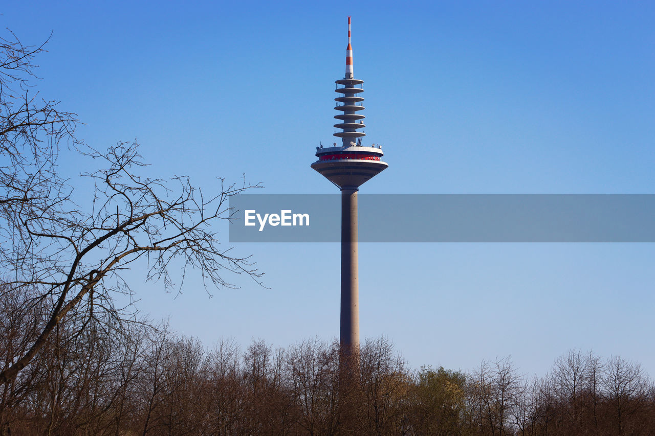 sky, tower, communications tower, architecture, clear sky, tree, nature, built structure, travel destinations, no people, blue, travel, plant, tourism, bare tree, low angle view, communication, city, building exterior, technology, outdoors, day, broadcasting, street light, spire, sunny, observation tower, building