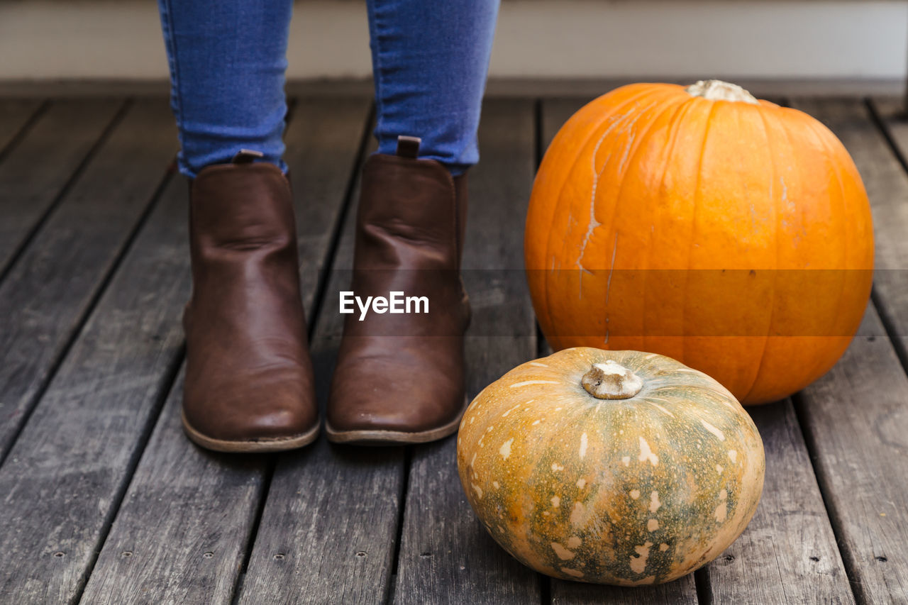 Low section of woman standing by pumpkins on hardwood floor