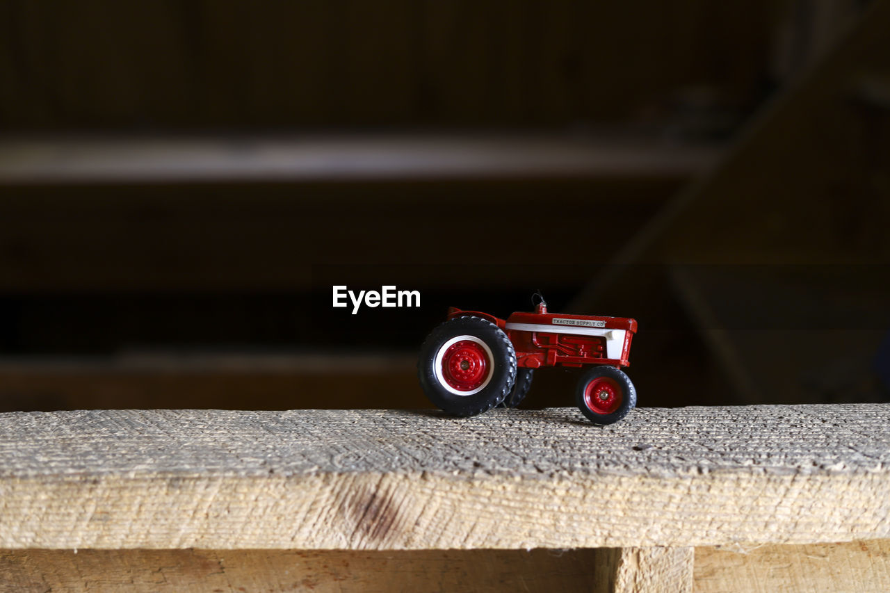 A red toy tractor on a ledge in a barn