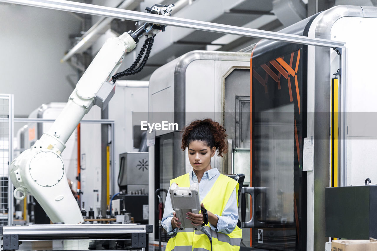 Young engineer controlling robotic arm with equipment in factory