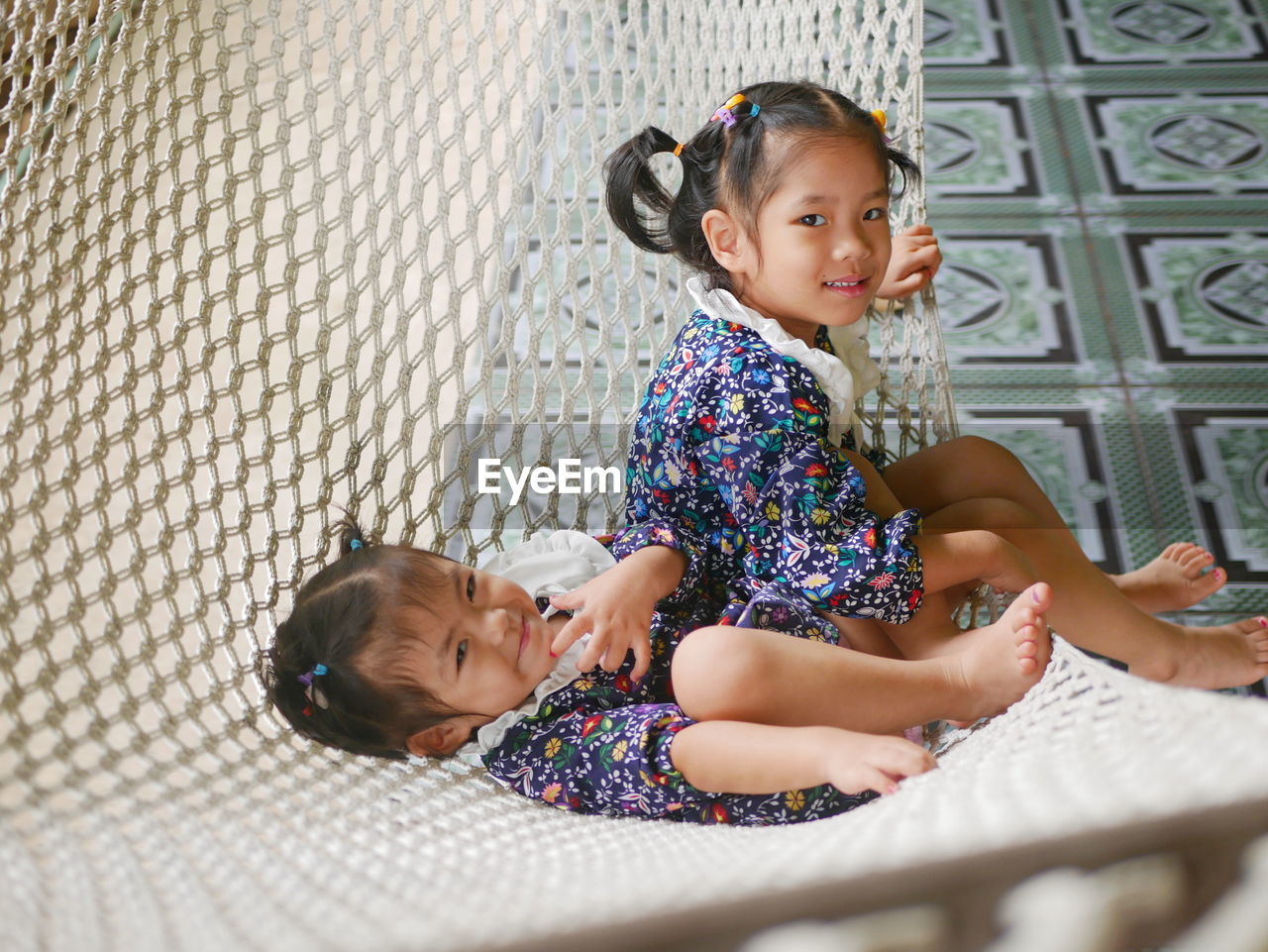 Happy asian baby girls, sisters, enjoys being together on a hammock - sibling relationship