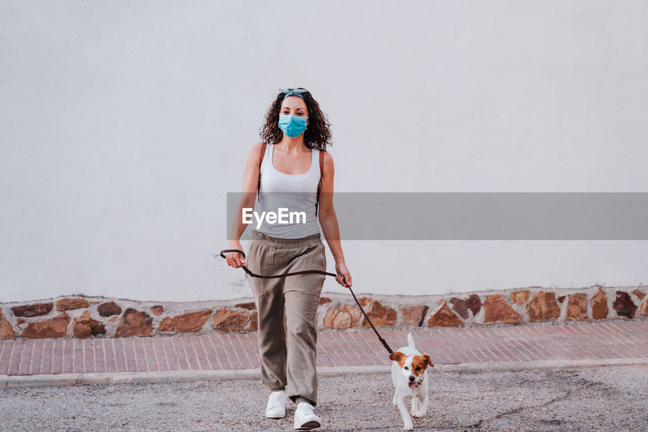 Full length of woman with dog walking against wall