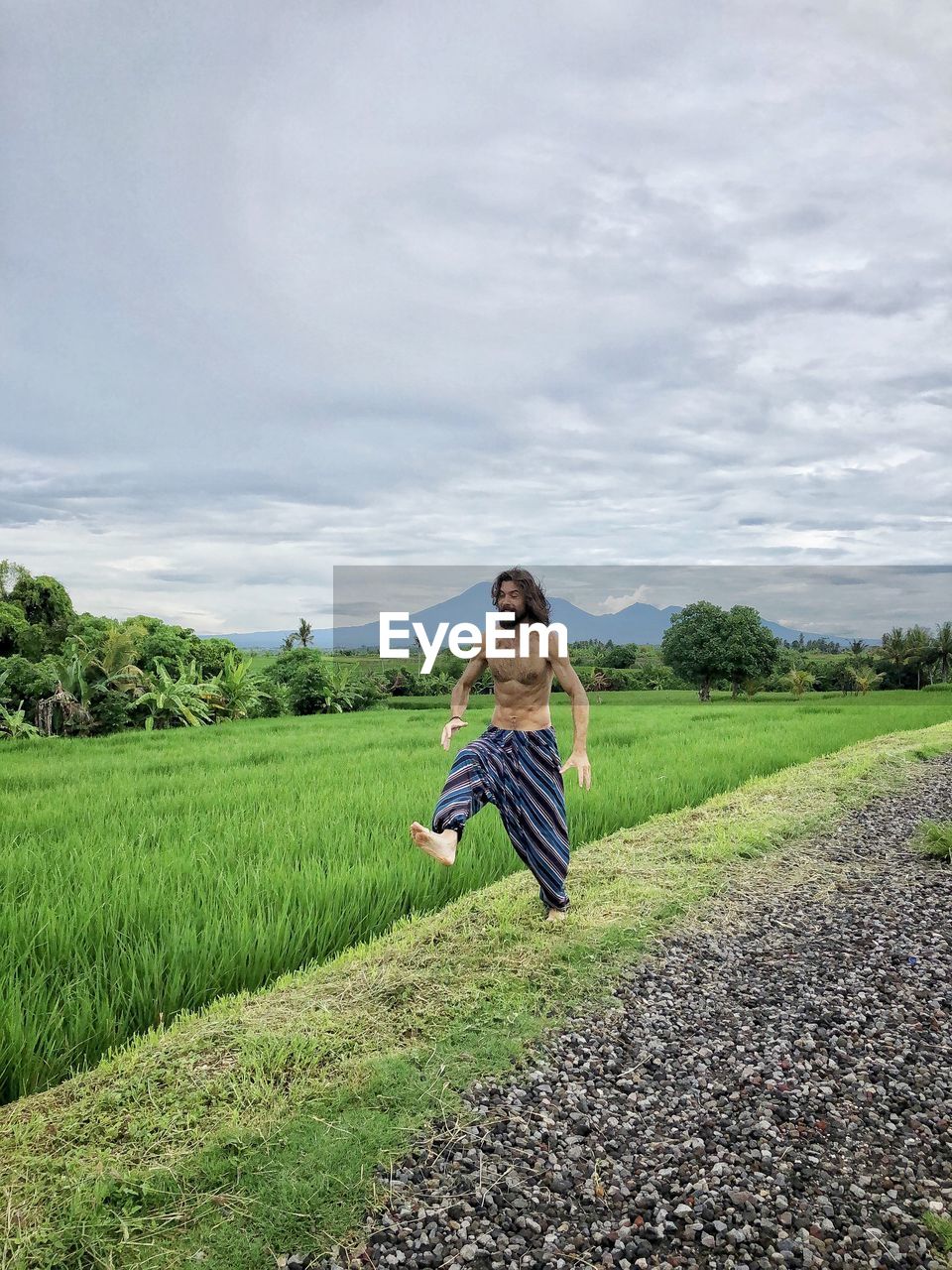 Shirtless man running on field against sky