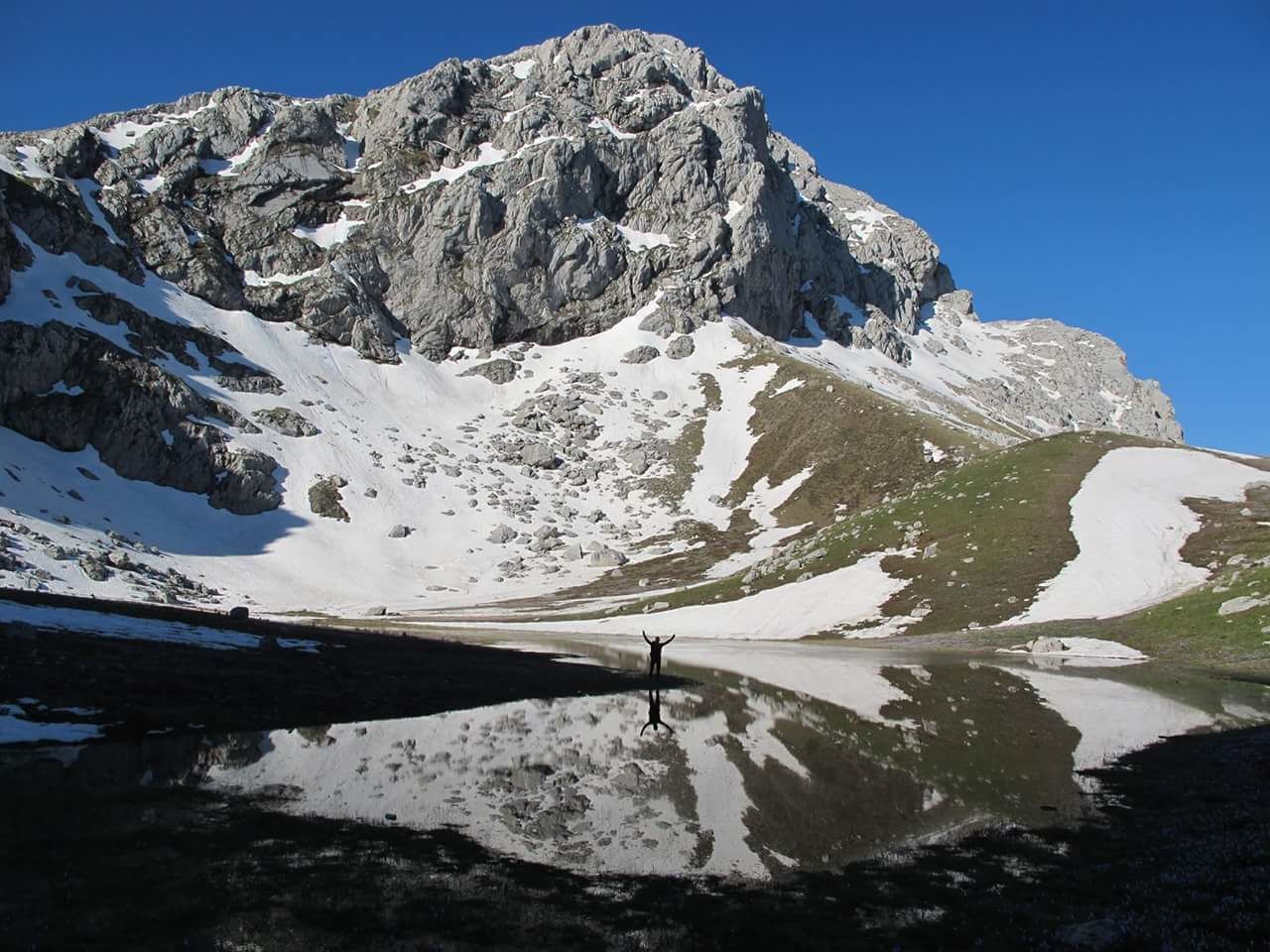 Mid distance view of person standing by lake against snowcapped mountain