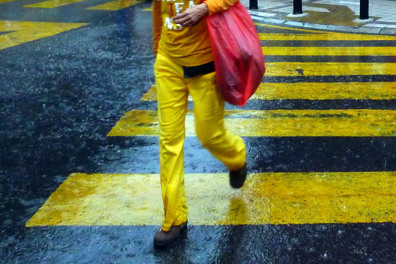 Low section of man walking on zebra crossing during rainy season