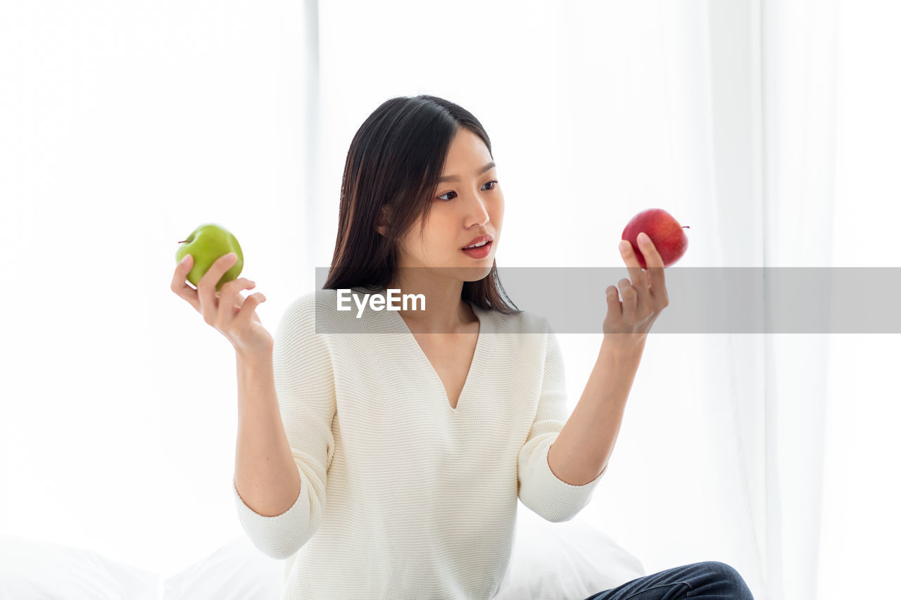 Smiling woman holding apples while sitting at home