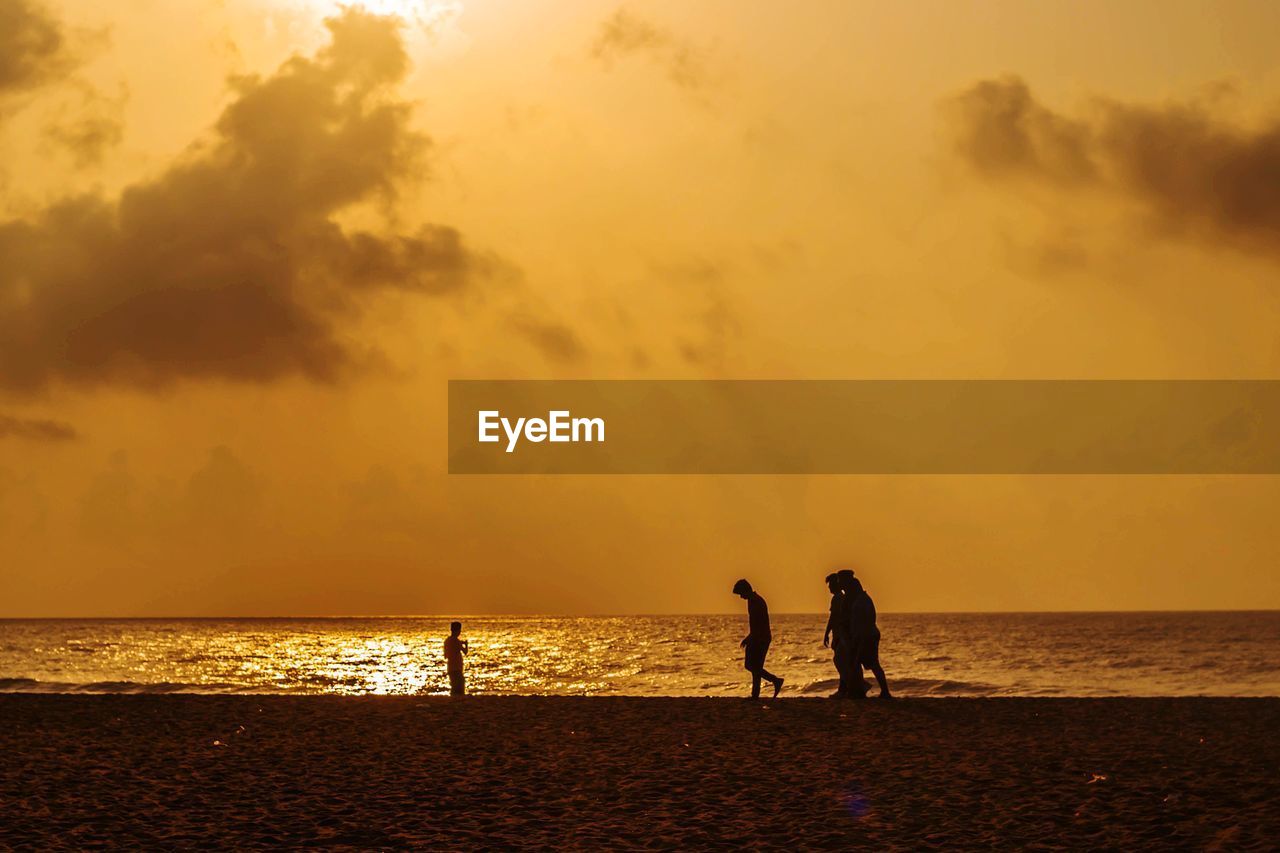 Silhouette people on beach against sky during sunset