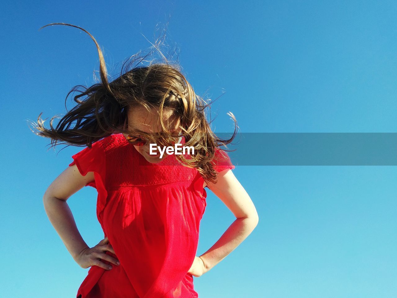 Low angle view of girl standing against clear blue sky