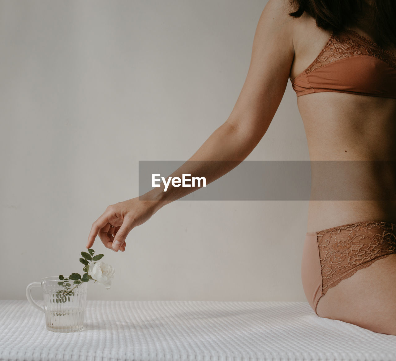Midsection of sensuous woman wearing lingerie and touching the flower