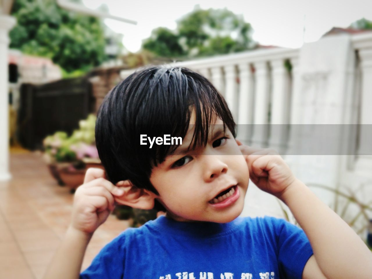 Close-up portrait of cute boy holding ears while standing outdoors