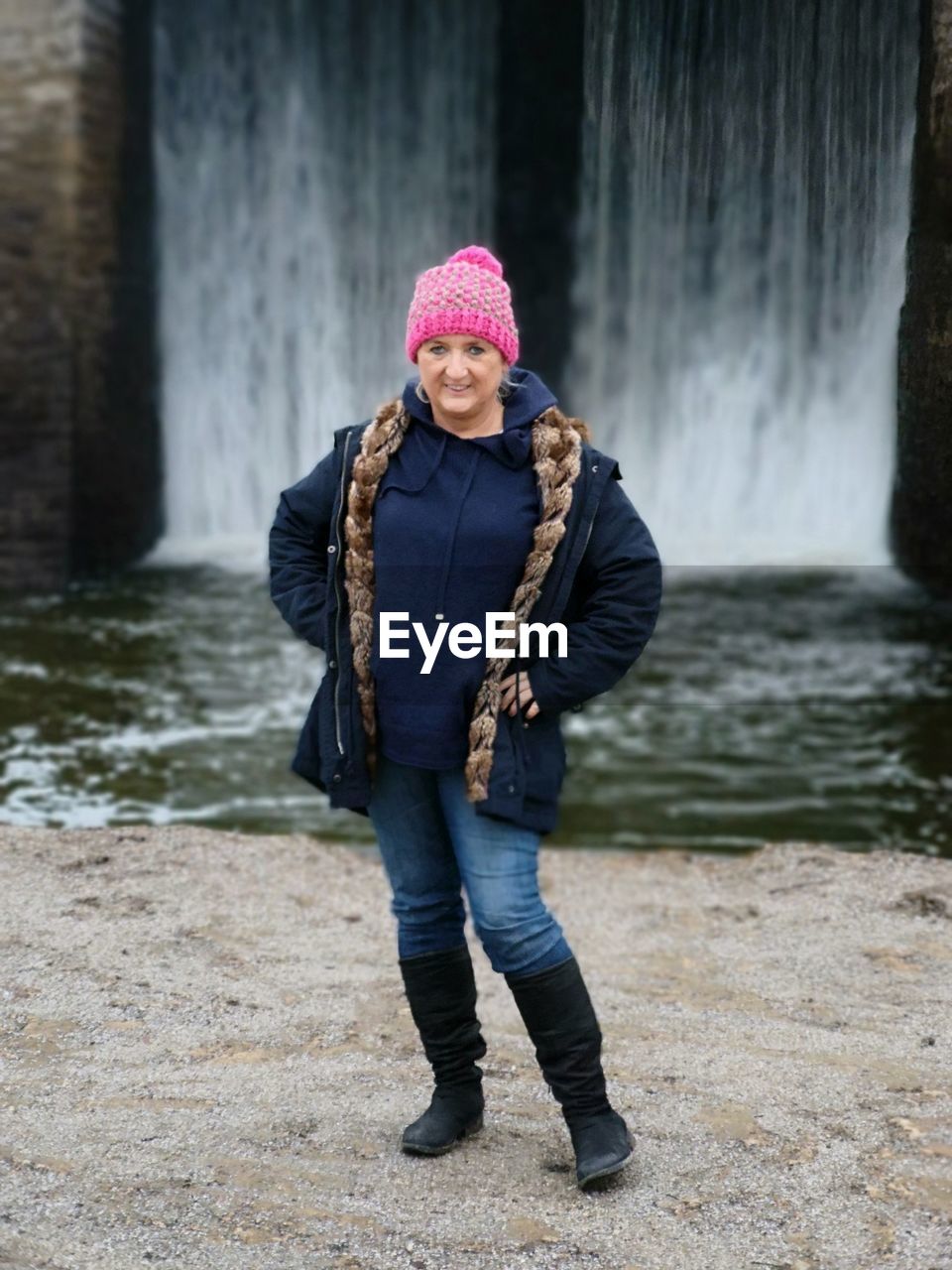 Full length portrait of smiling woman standing against waterfall