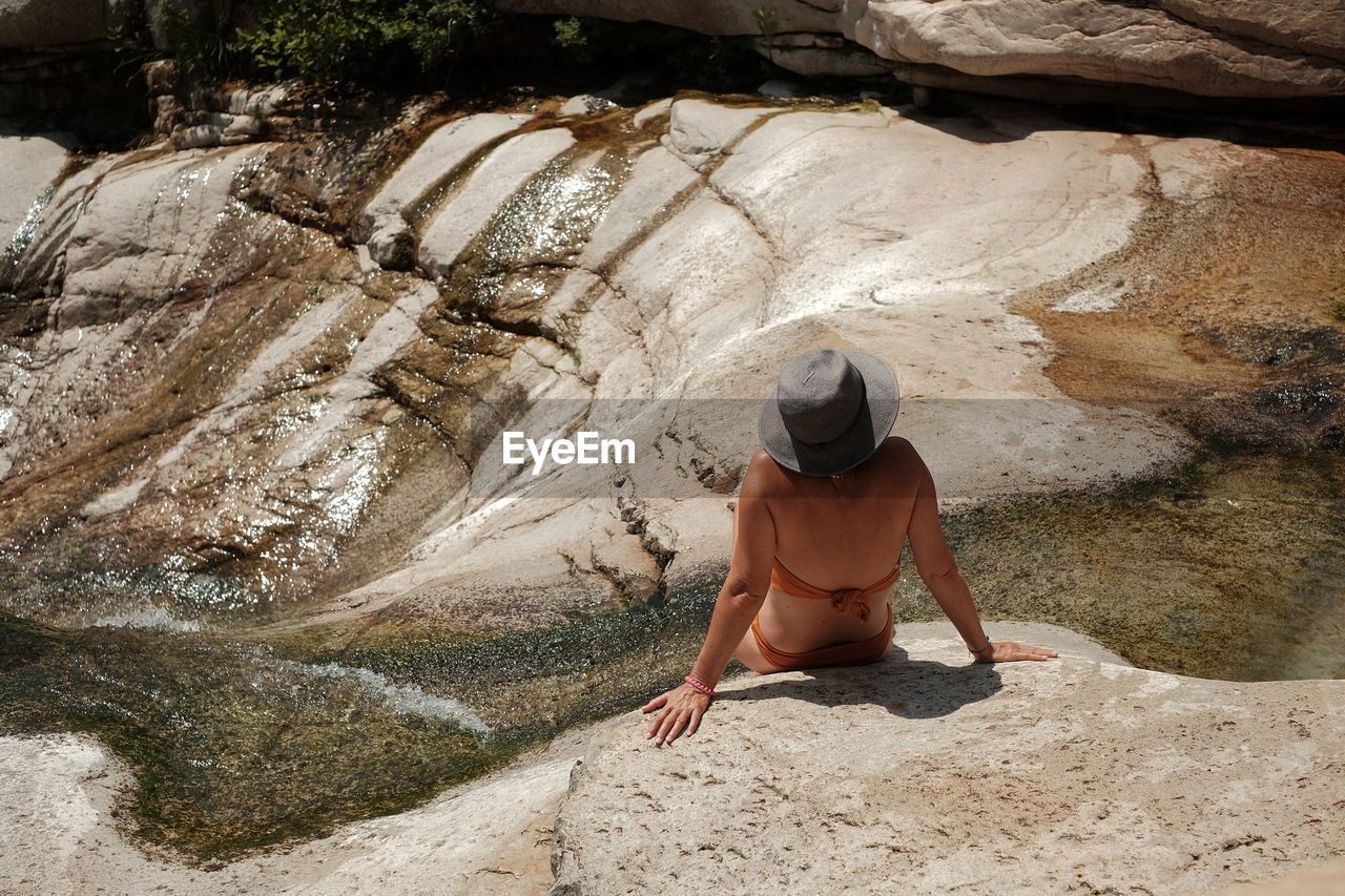 Rear view of woman wearing bikini while sitting on rock
