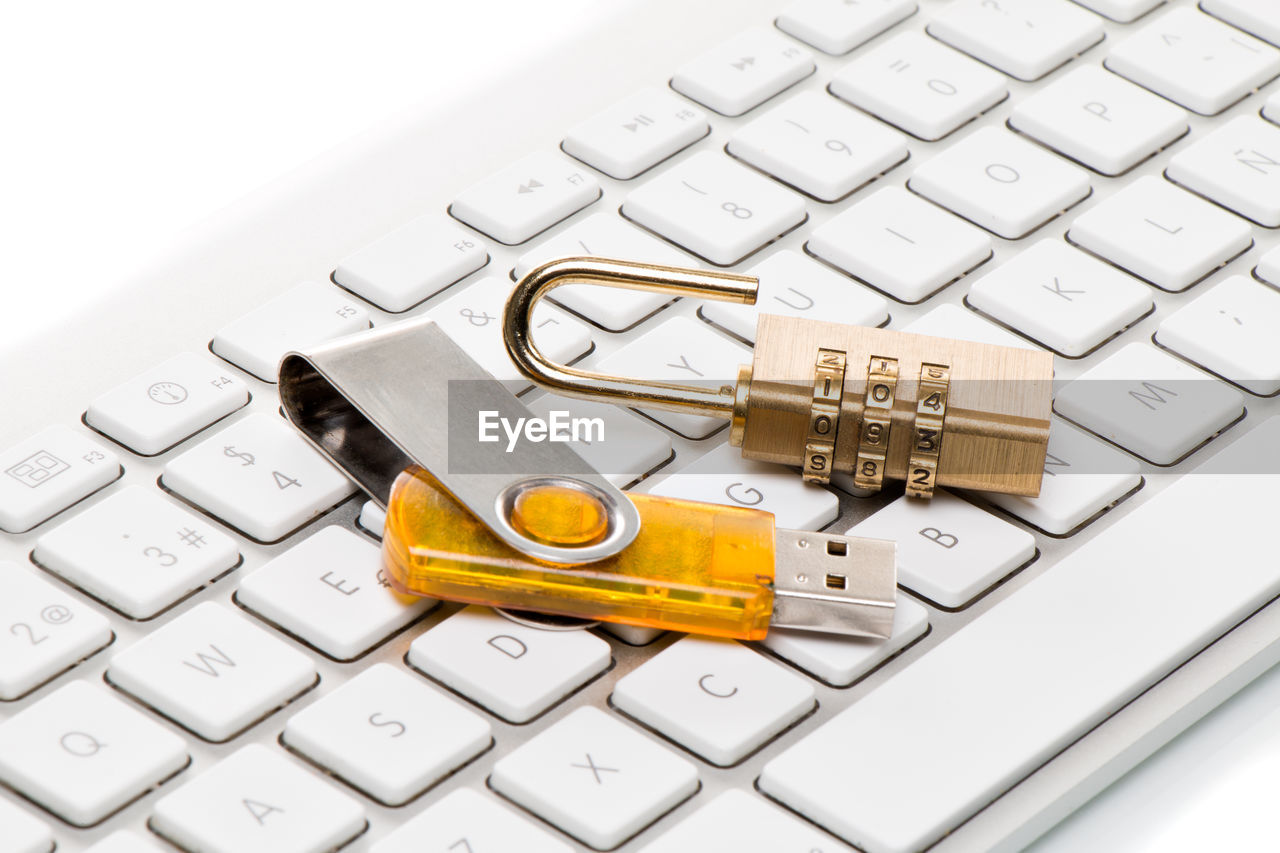 Close-up of padlock and usb stick on computer keyboard against white background