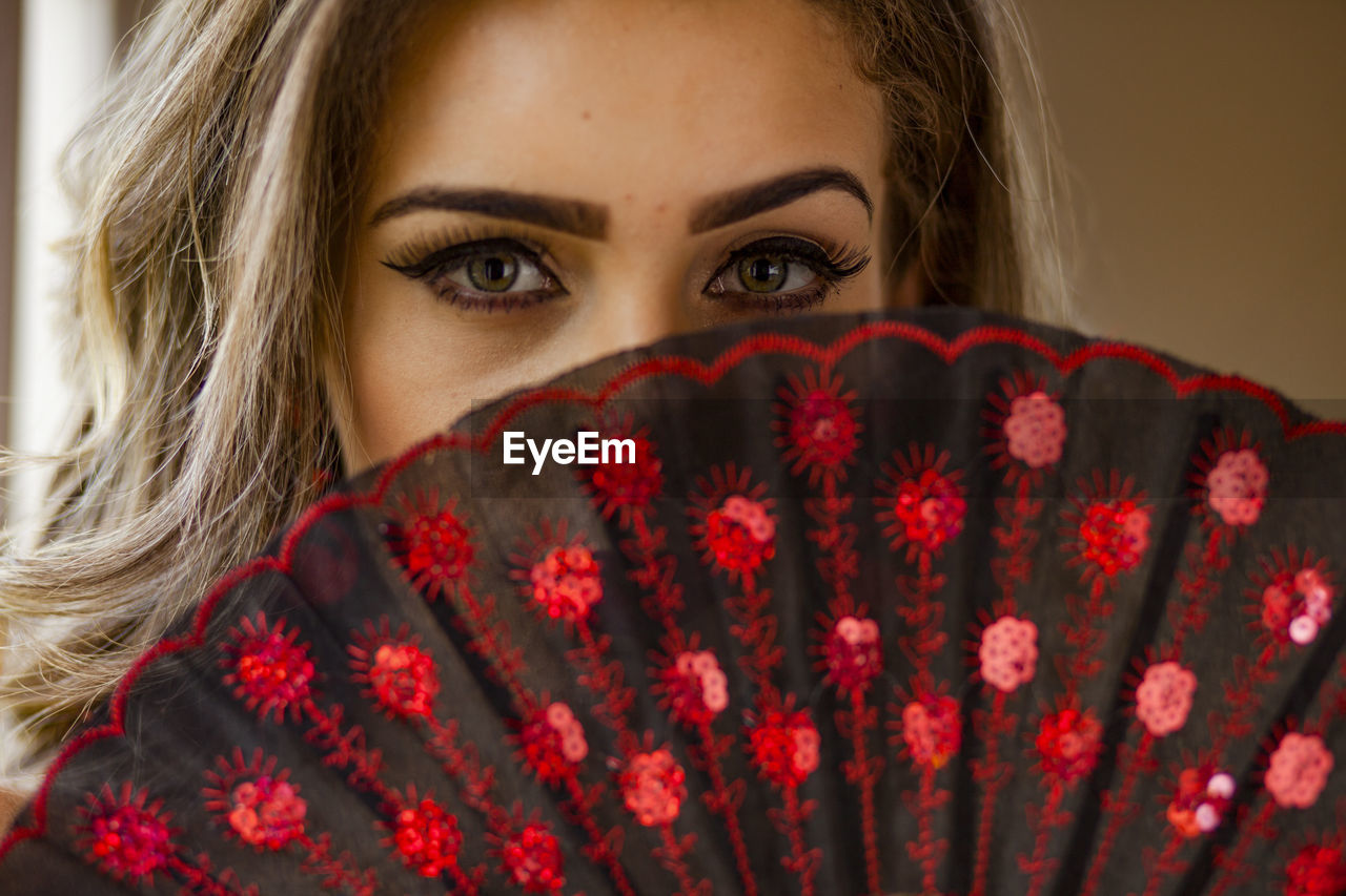 Close-up portrait of woman covering face with hand fan
