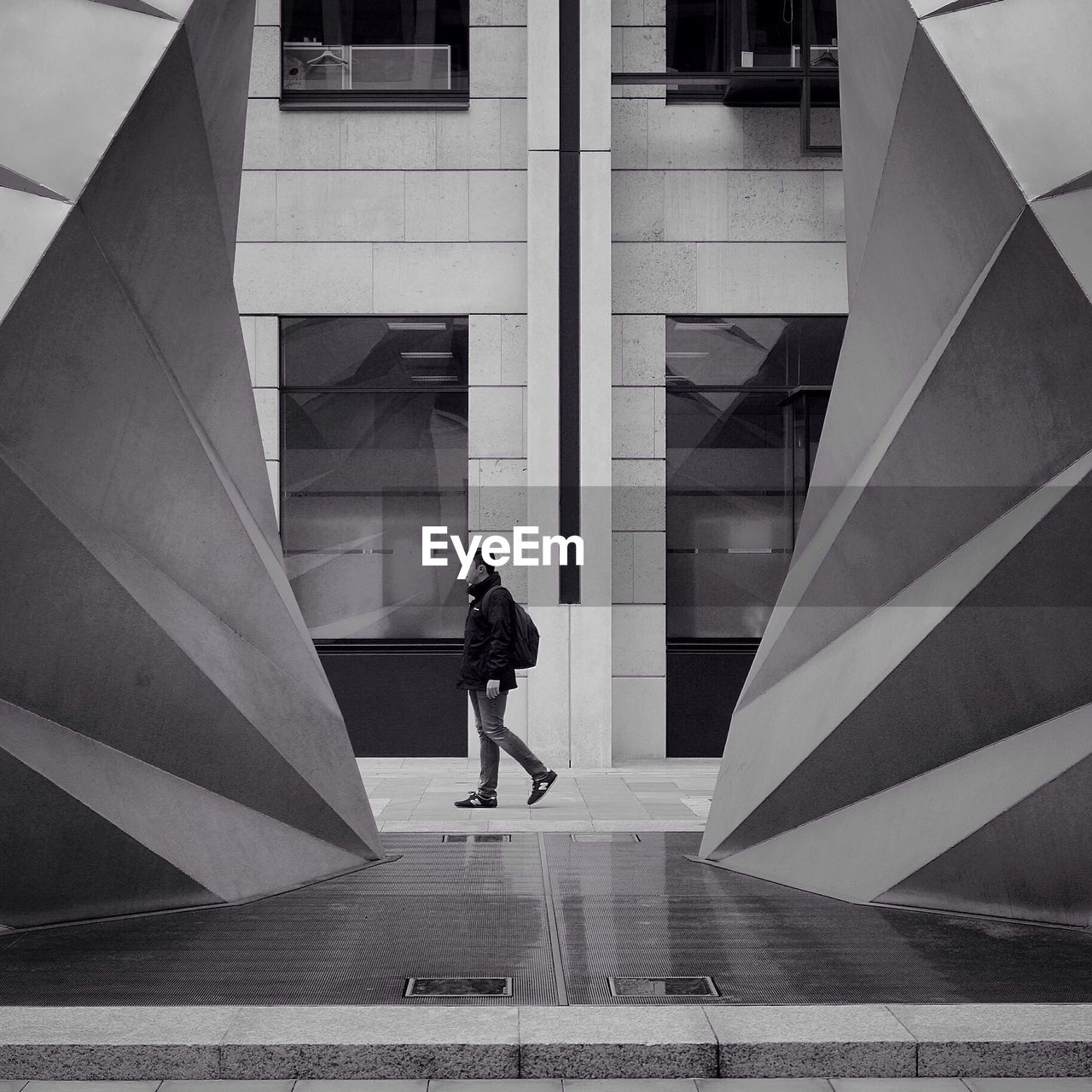 Full length side view of young man walking on footpath against building