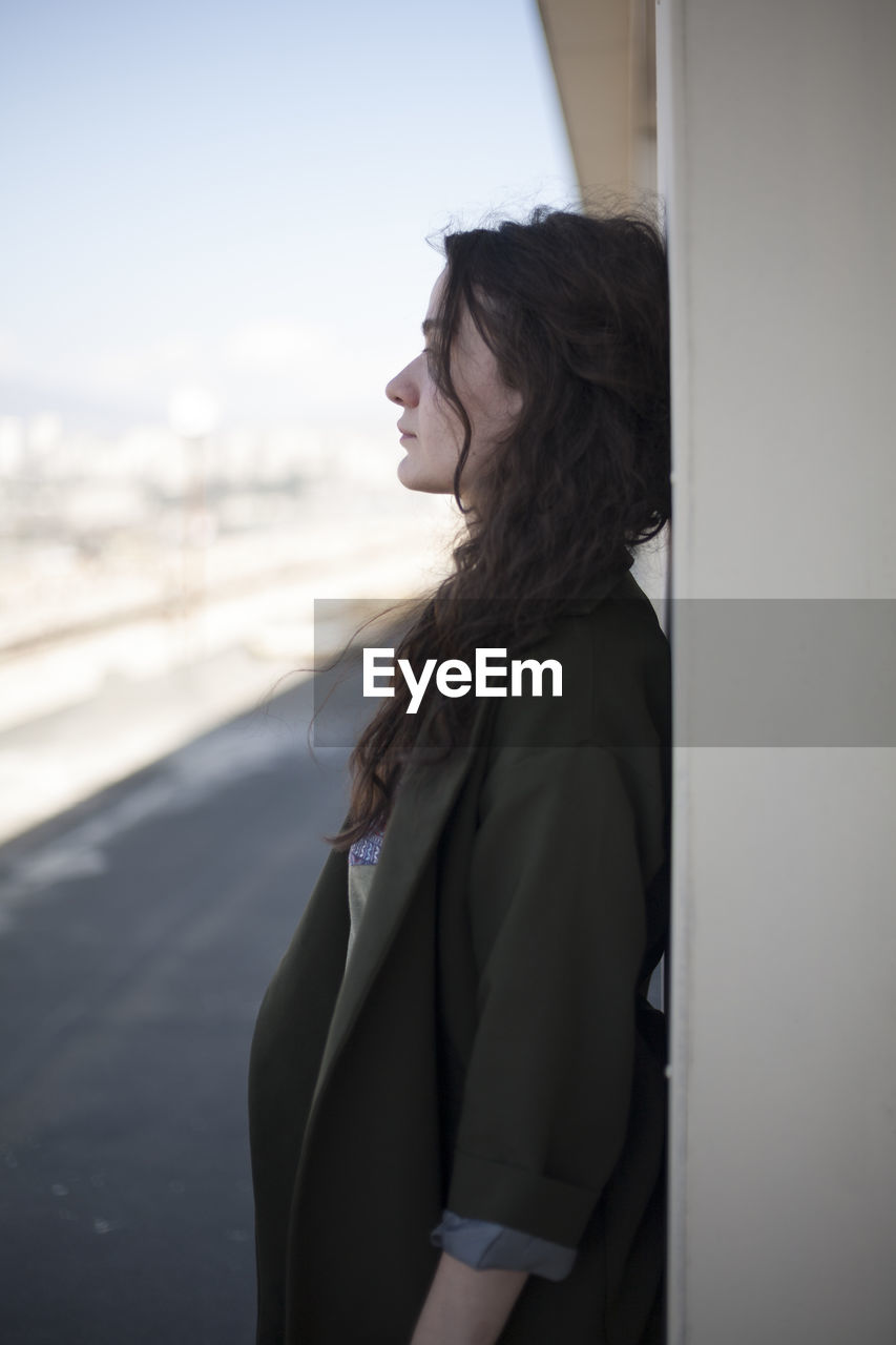 Side view of young woman standing by wall