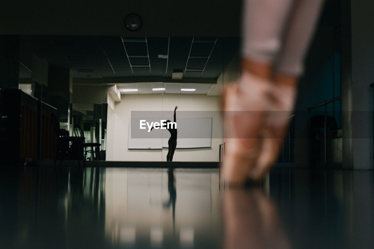 Low section of woman practicing ballet with reflection in mirror at dance studio