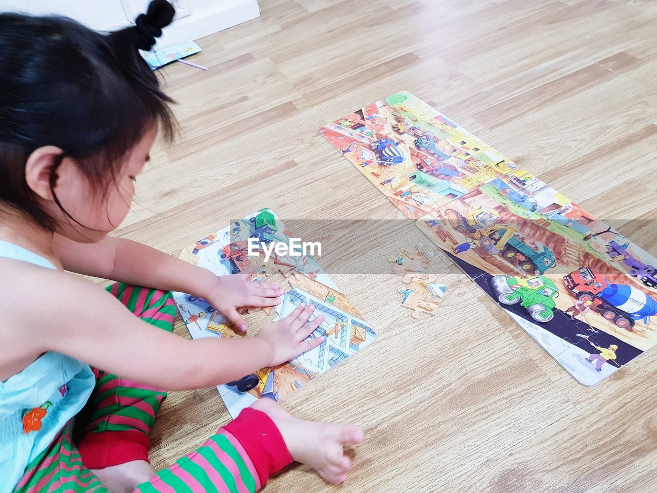 High angle view of cute girl playing with puzzles while sitting on hardwood floor at home