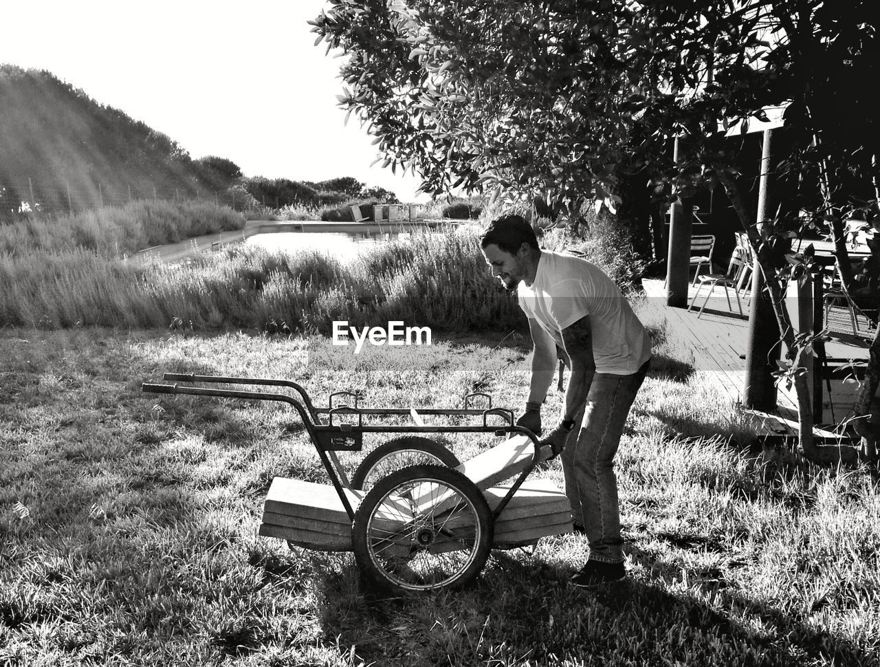 Side view of young man placing tiles on push cart at grassy field