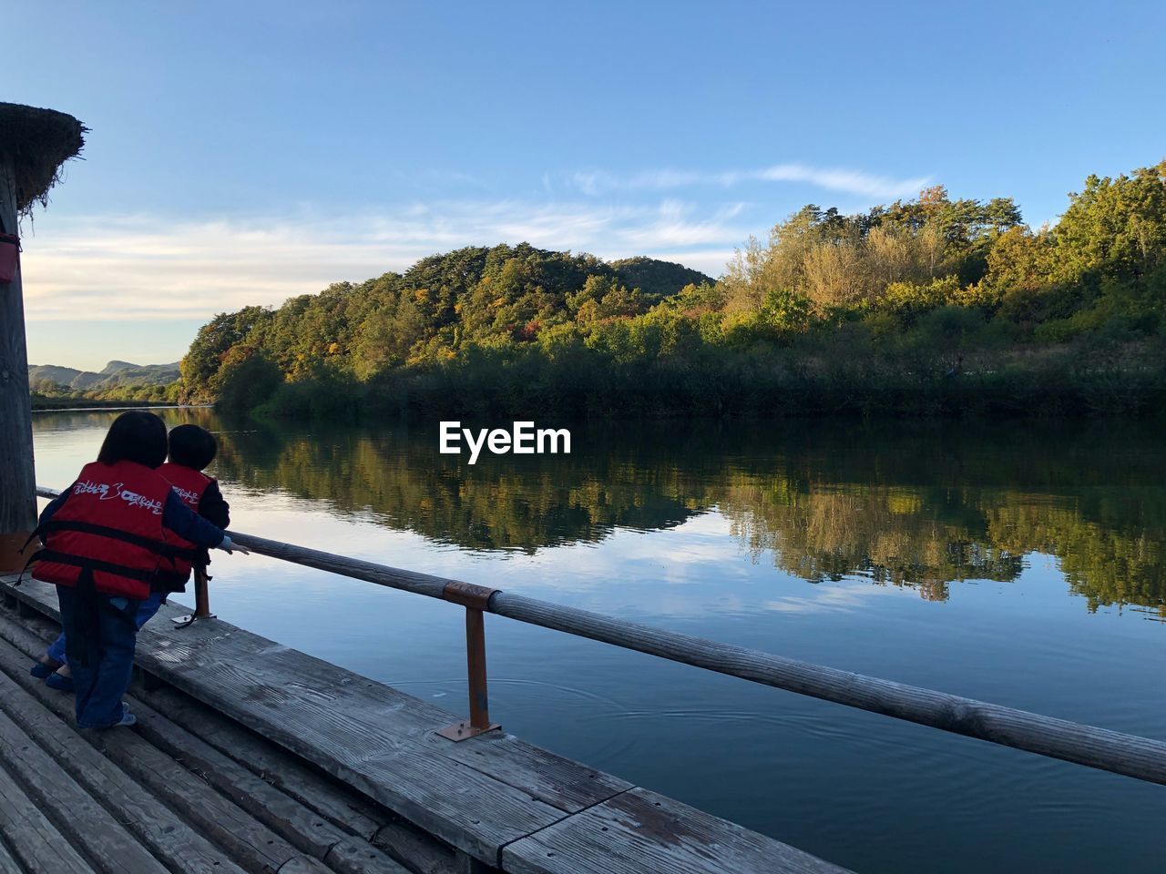 REAR VIEW OF MEN SITTING ON LAKE AGAINST SKY