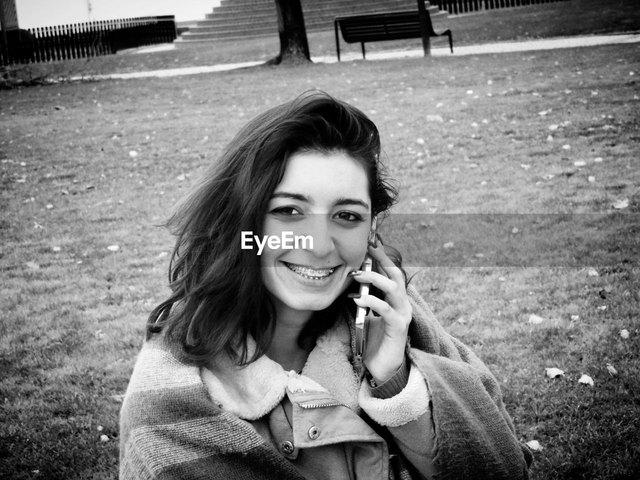 Portrait of smiling young woman talking on mobile phone while standing at park