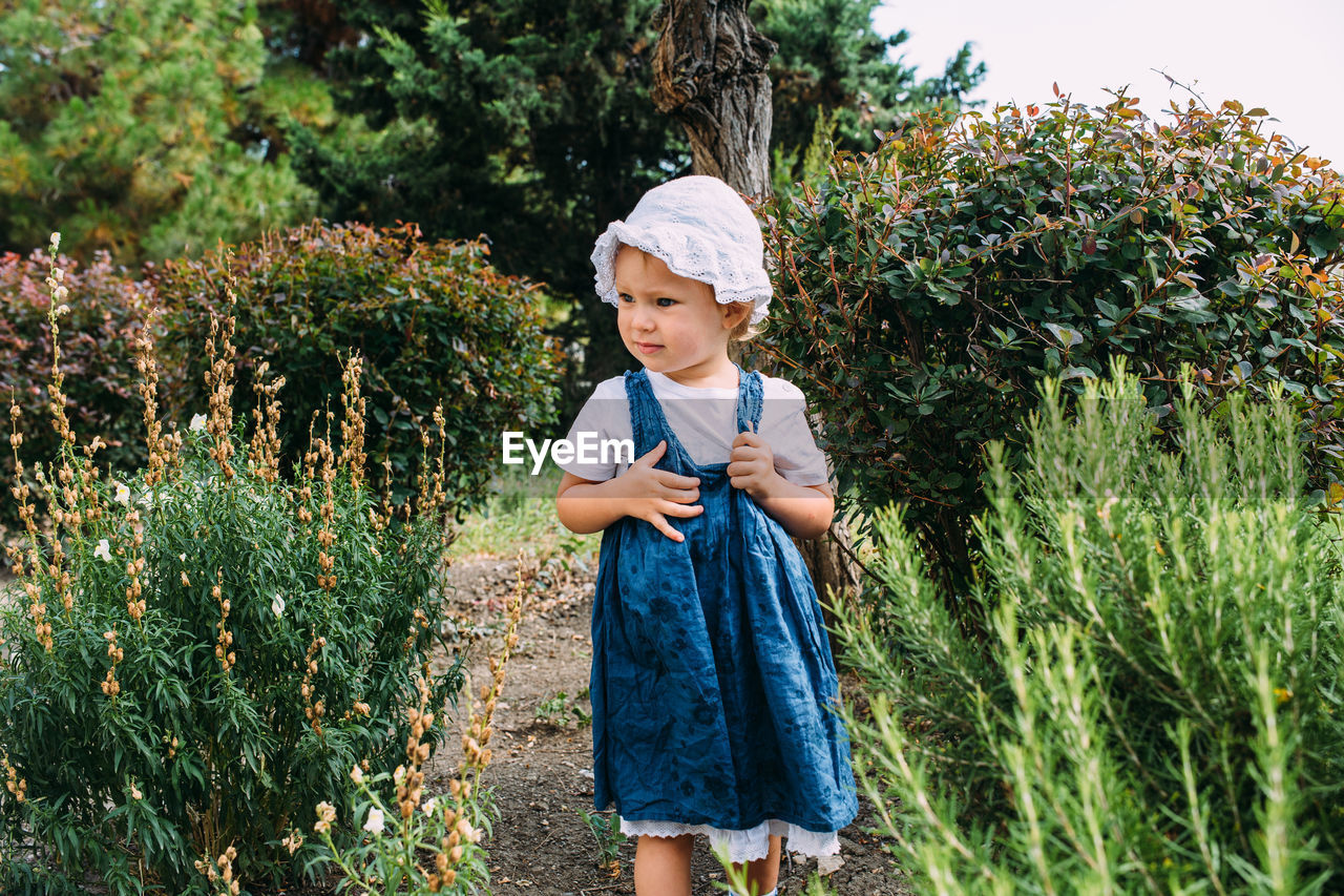 Little girl walks in the garden among beautiful evergreen southern plants