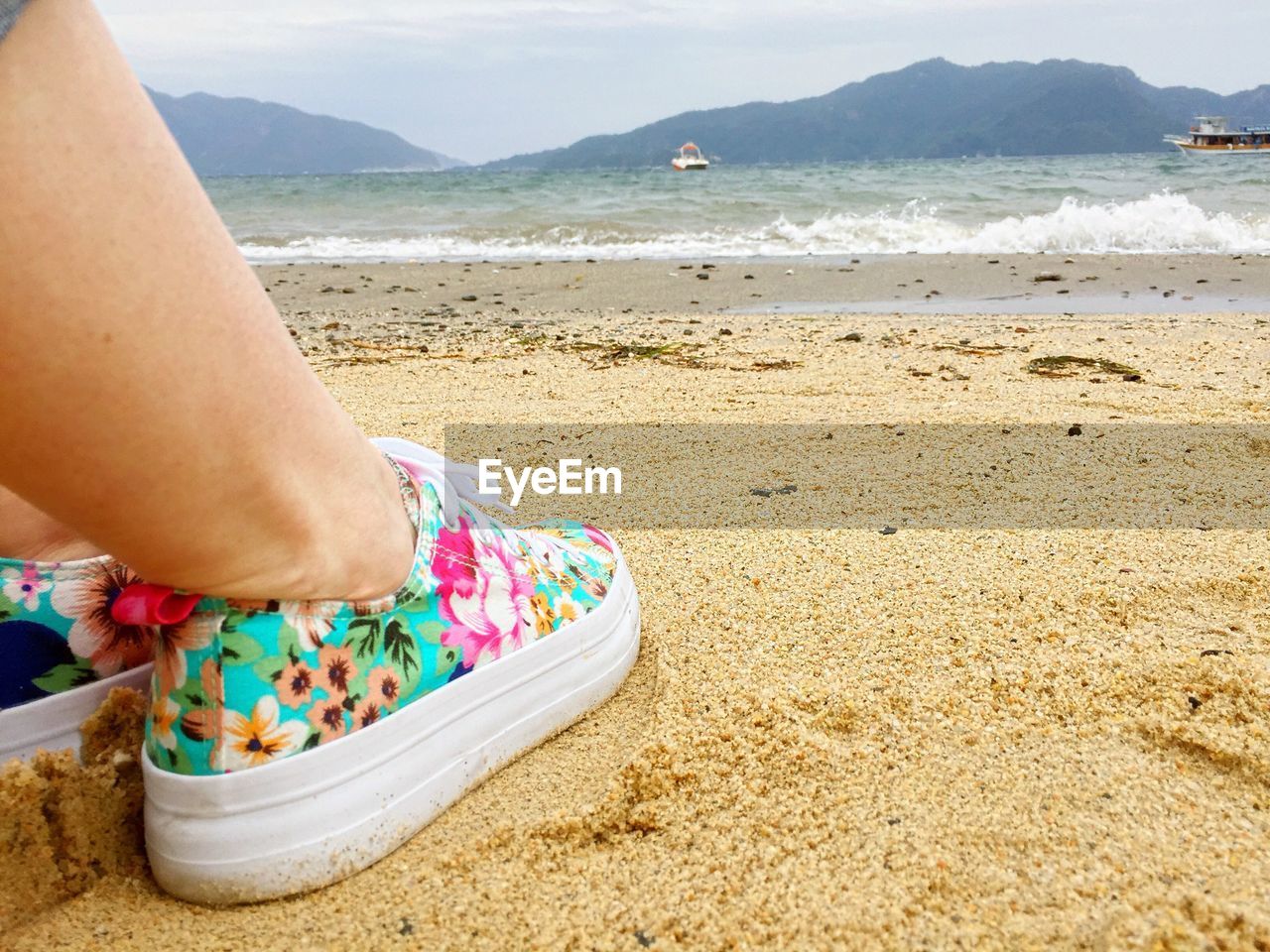 Low section of person wearing colorful shoes on sandy beach