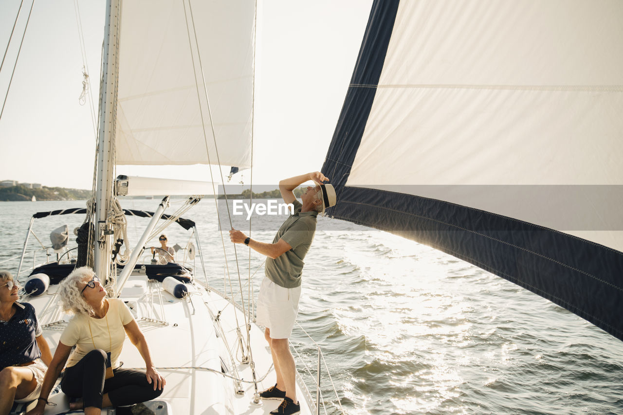 Senior man looking up while standing by female friends in boat on sunny day