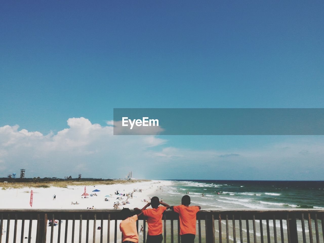 Rear view of boys standing on pier at beach against sky