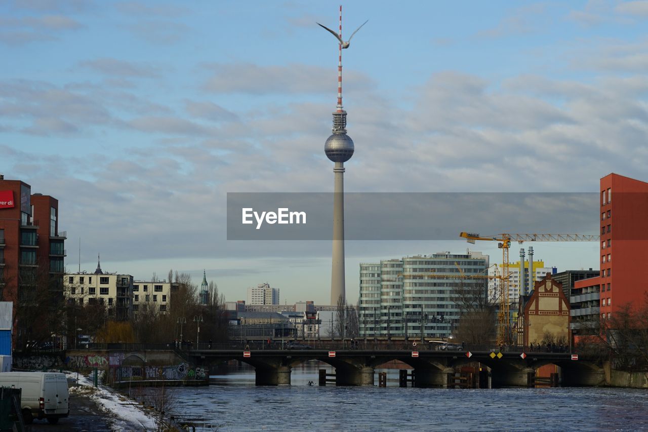 Low angle view of fernsehturm and buildings by river against sky