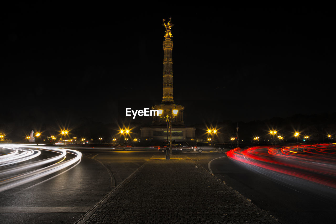 Statue by light trails on road at night