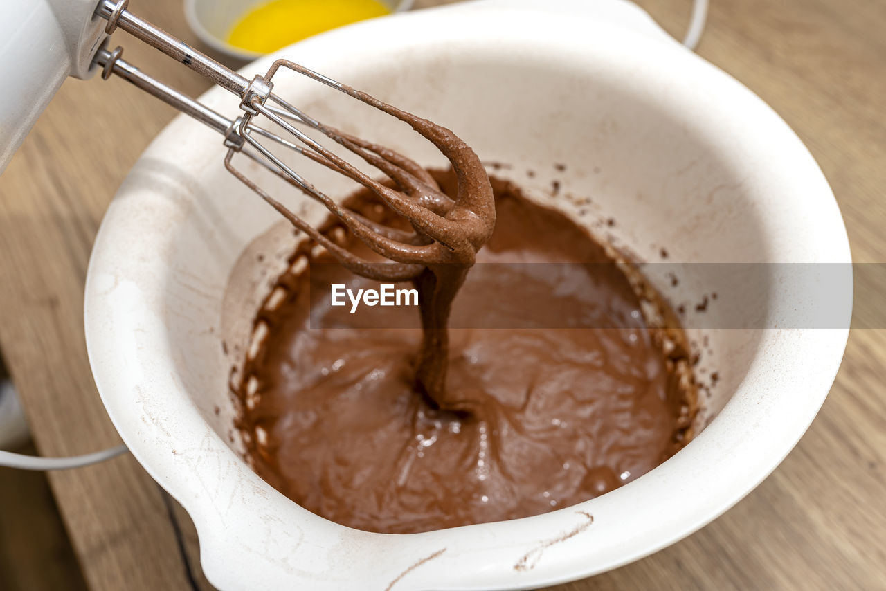 Hand mixer with a whisk raised above the bowl, with raw dough, the dough is in a thick  brown state.