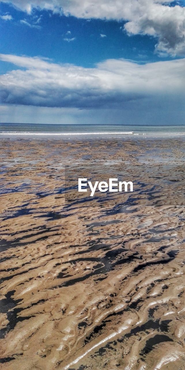 Scenic view of wet shore at beach against sky