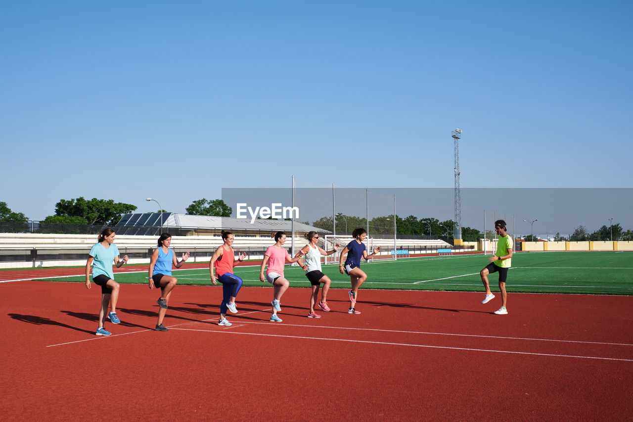 Group of women practice pre-workout stretching with their young traine