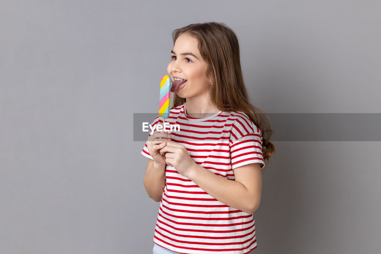 striped, one person, studio shot, indoors, gray background, women, photo shoot, gray, clothing, casual clothing, portrait, person, teenager, adult, young adult, smiling, emotion, happiness, waist up, holding, copy space, hand, hairstyle, human face, standing, child, long hair, arm, female, pink, childhood, lifestyles, brown hair, looking, finger, positive emotion, portrait photography, looking at camera, white background, relaxation, front view, t-shirt, colored background