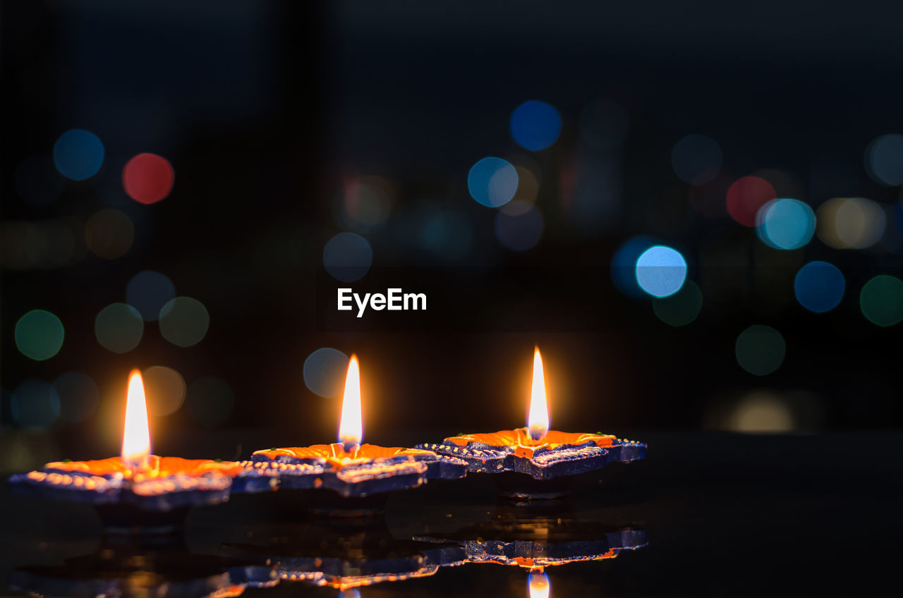Clay diya lamps lit on dark background with colorful bokeh lights. diwali festival concept.