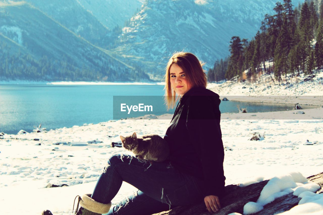 Young woman sitting on land by sea during winter