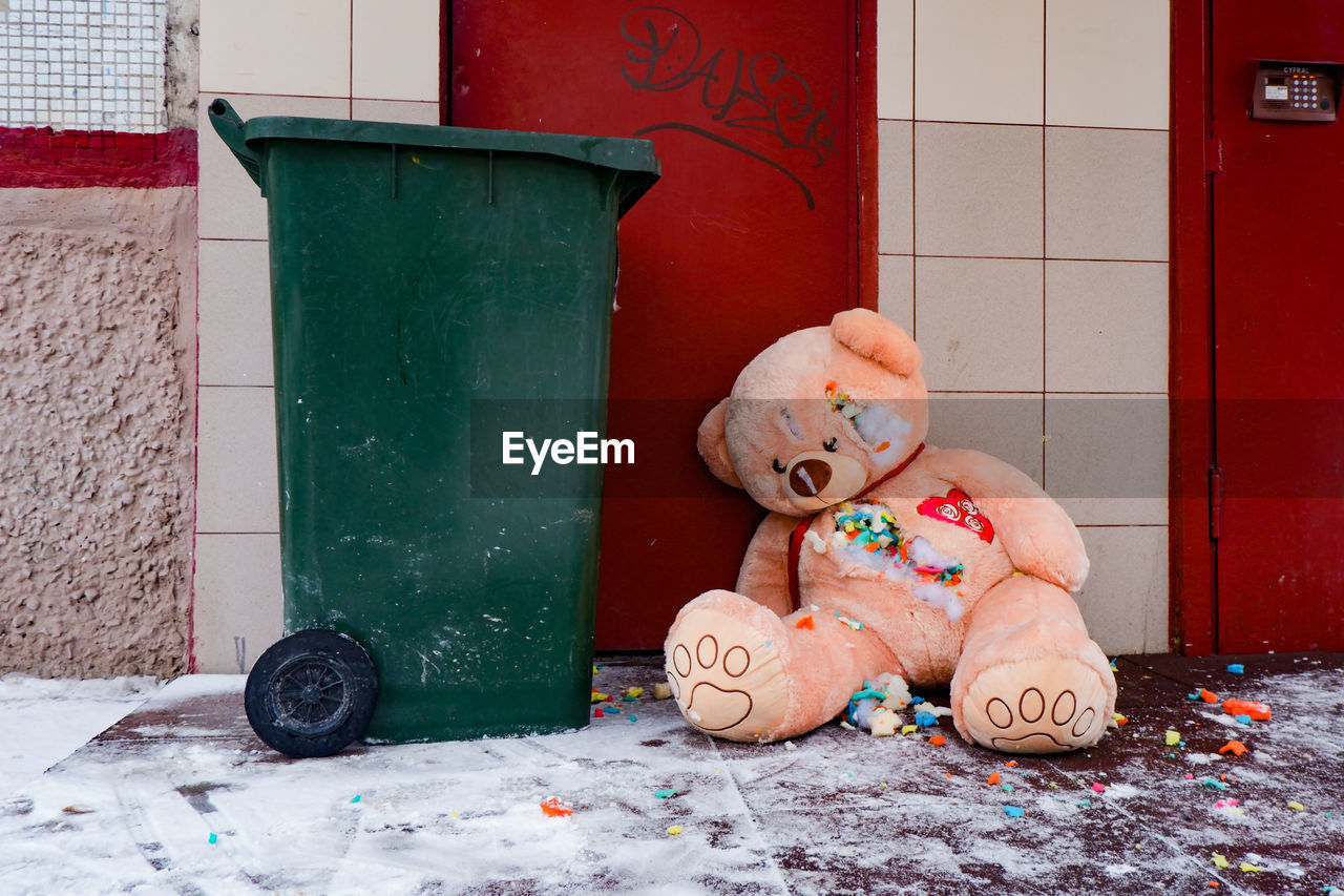 A gutted stuffed teddy bear lies torn apart by a dumpster