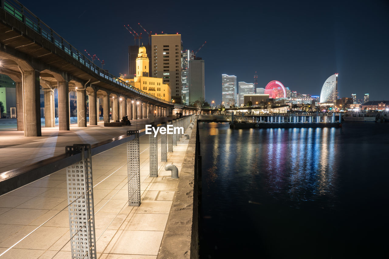 Illuminated buildings by river against sky at night