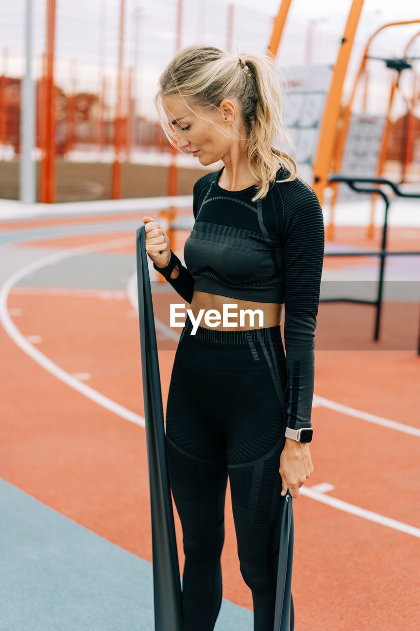 Young athletic woman is training on the sports ground using sports elastic bands.