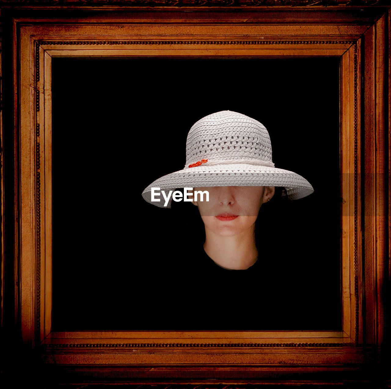 Woman wearing white sun hat seen from wooden picture frame against black background