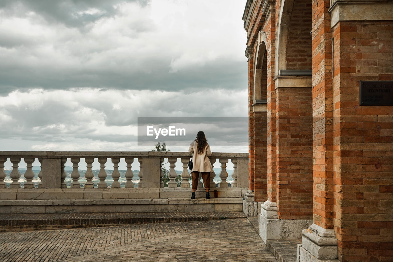Rear view of women standing on railing against cloudy sky in treia