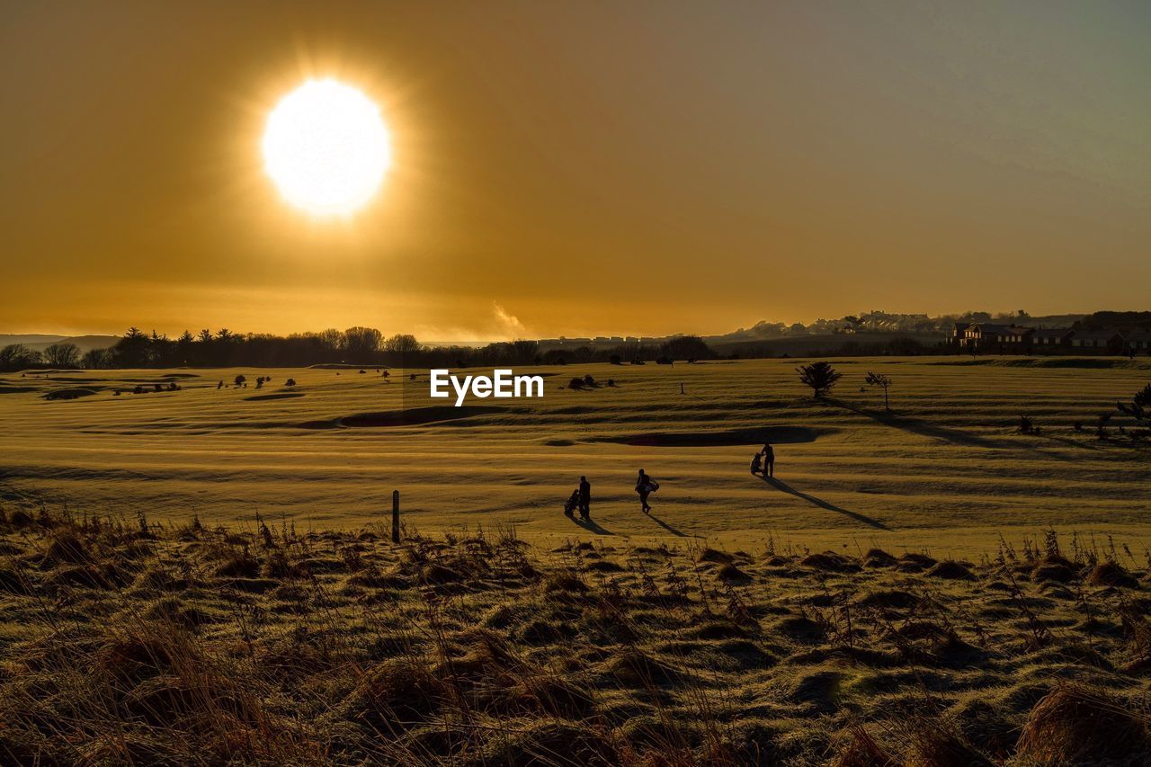 High angle view of people walking on golf course during sunset