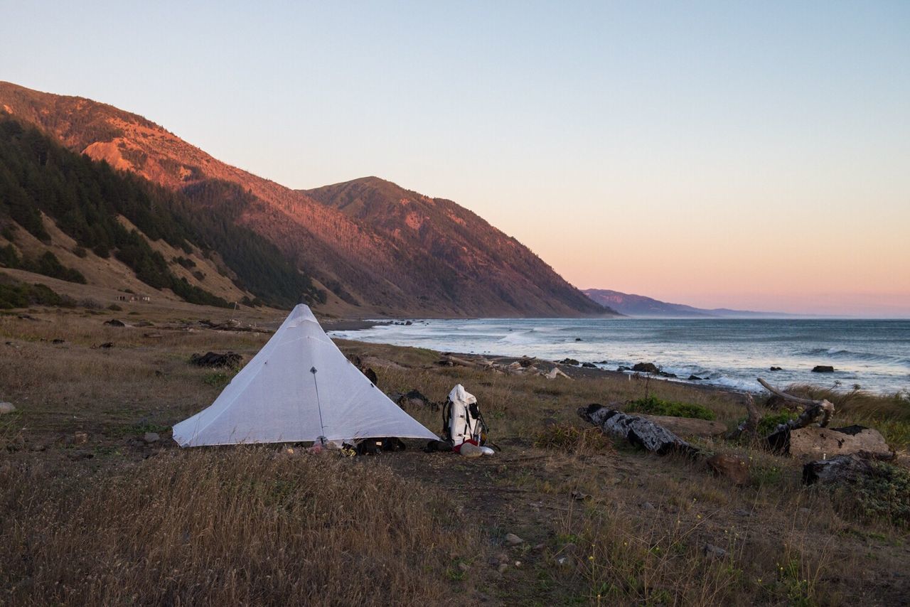 Tent on beach by mountains against clear sky during sunset