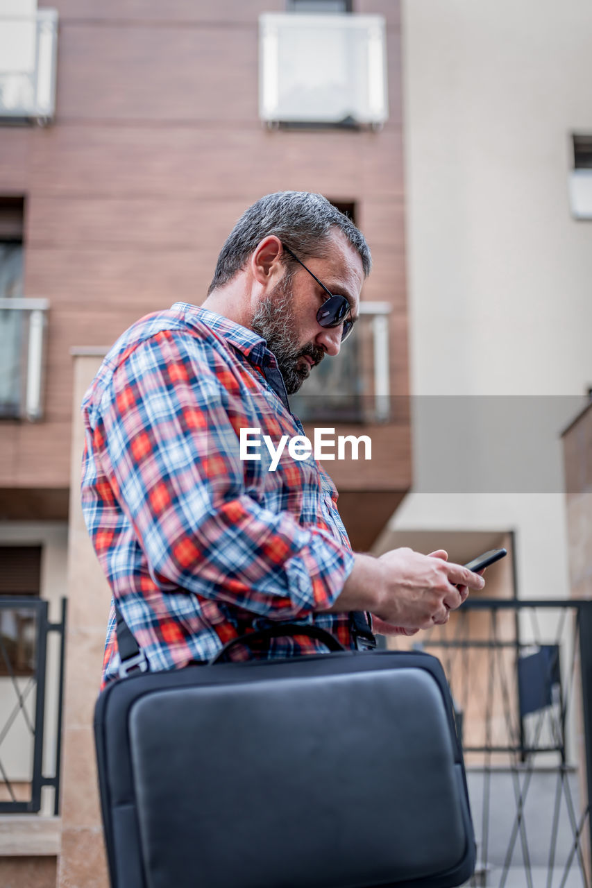 Portrait of handsome businessman with sunglasses and plaid shirt walking  and typing messages