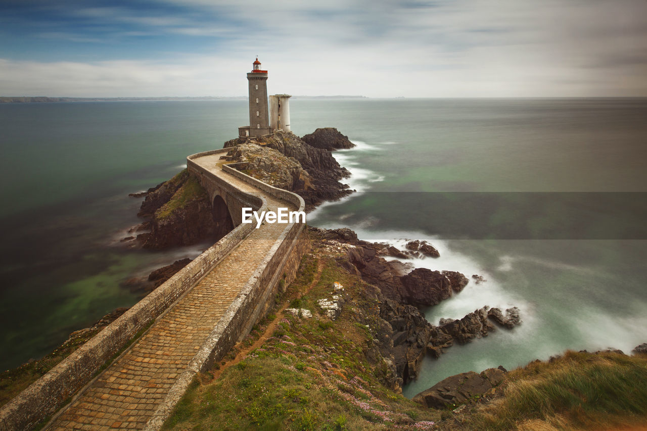 Lighthouse on pier by sea against sky