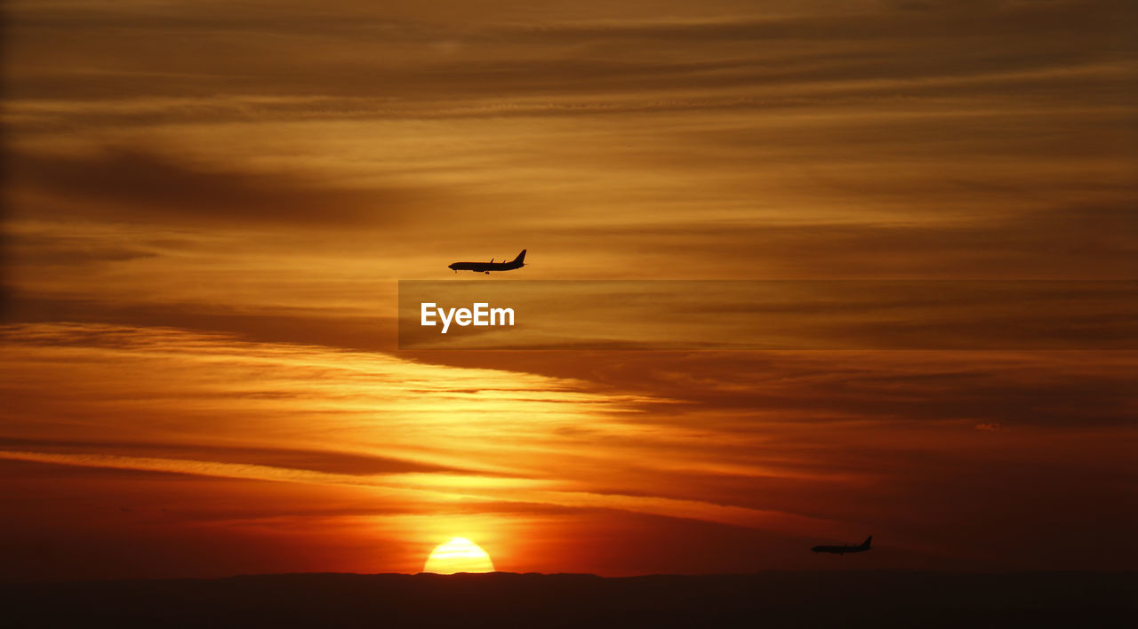 Silhouette plane flying in sky during sunset