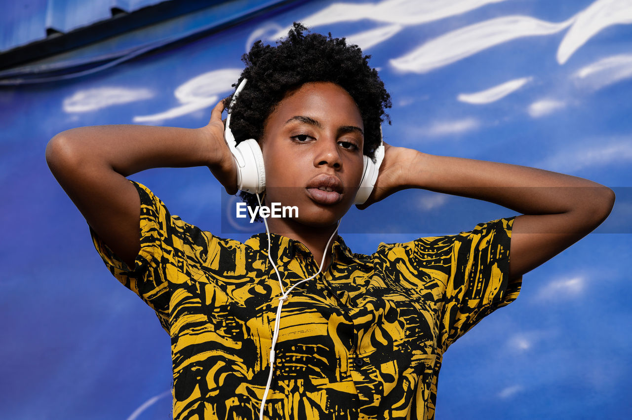 Young african american woman with short hair and modern clothes listening to music with headphones